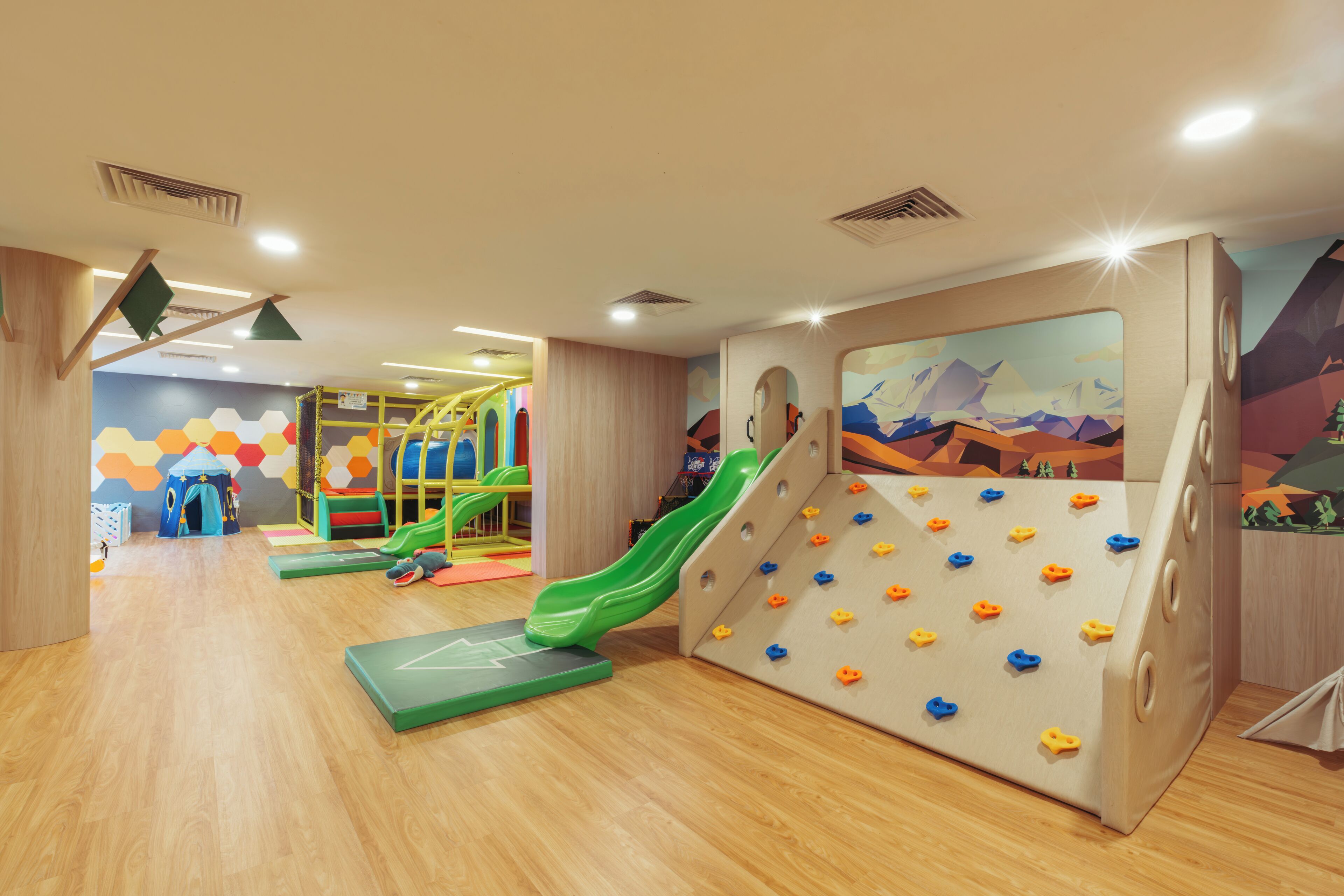 A play area with a slide, climbing wall, and colorful hexagonal wall art.