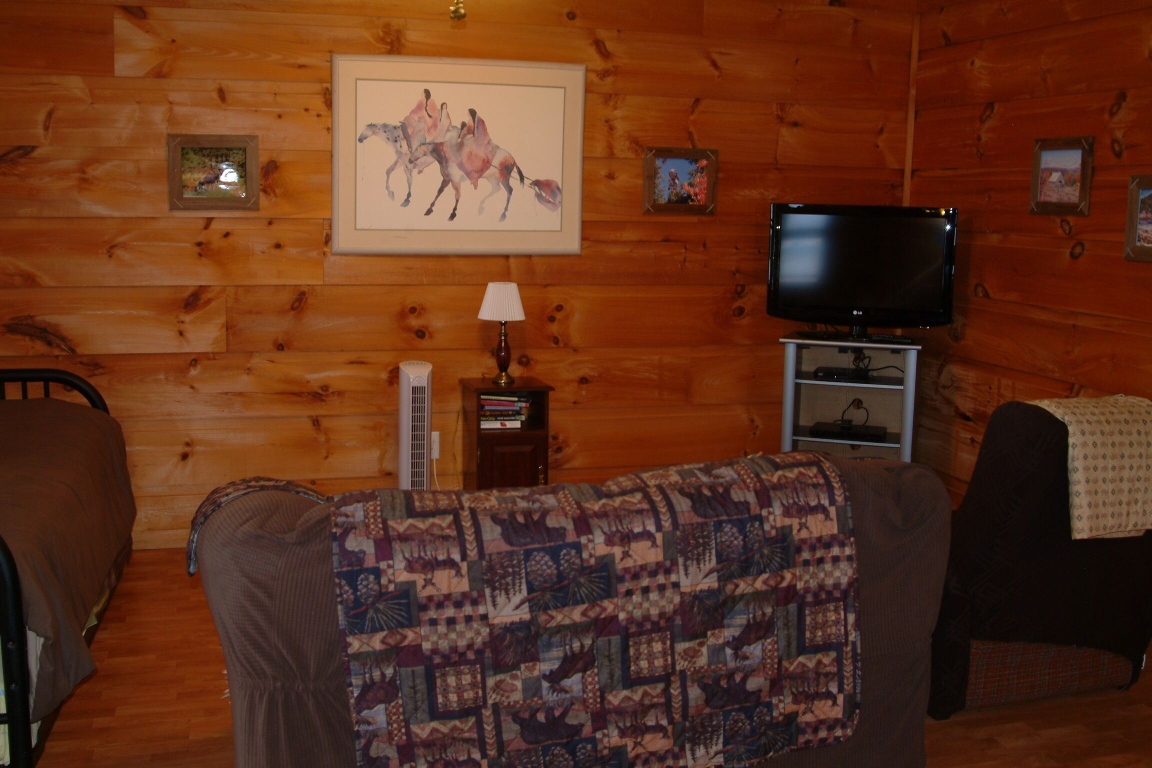A wooden-paneled room with a television, a framed horse painting, and a quilted blanket on a couch.