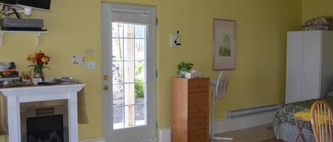Une pièce avec une cheminée, une porte donnant sur l’extérieur, une commode en bois, un lit recouvert d’une couvre-lit à motifs et une chaise.