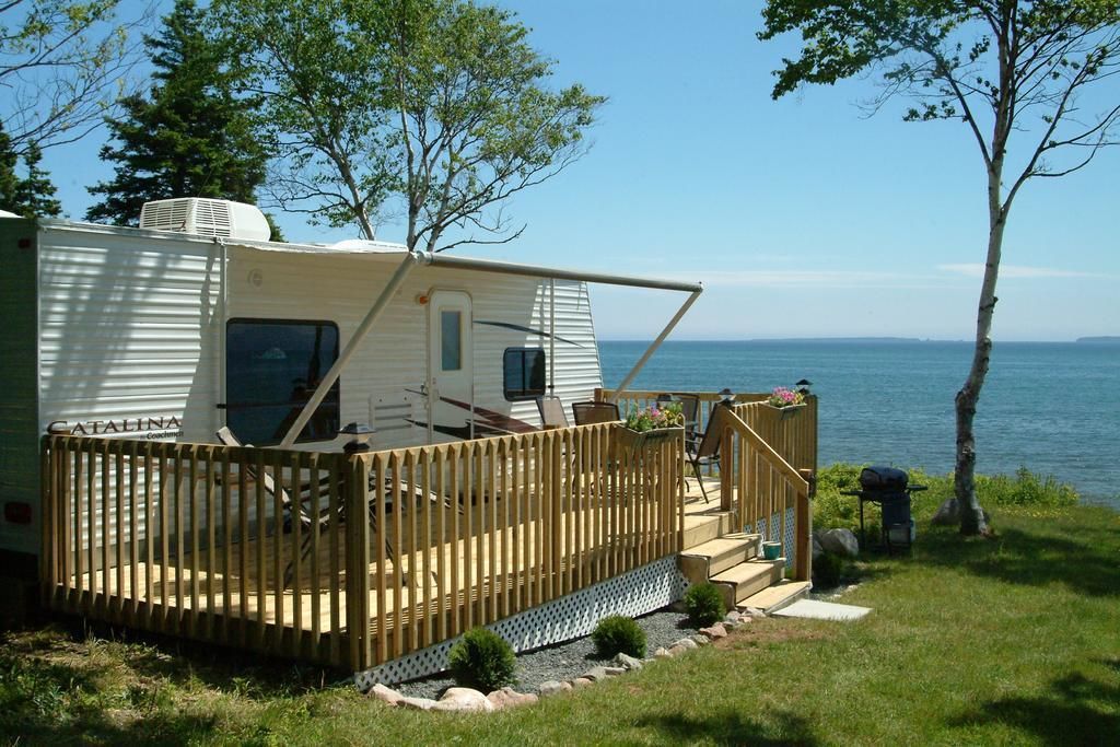 A recreational vehicle with a deck and outdoor seating area, situated by a body of water.