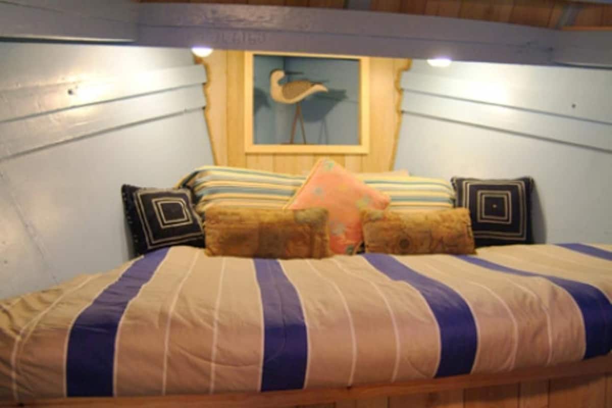 A bed with striped bedding and multiple pillows, a framed picture on the wall, and wooden paneling on the walls.