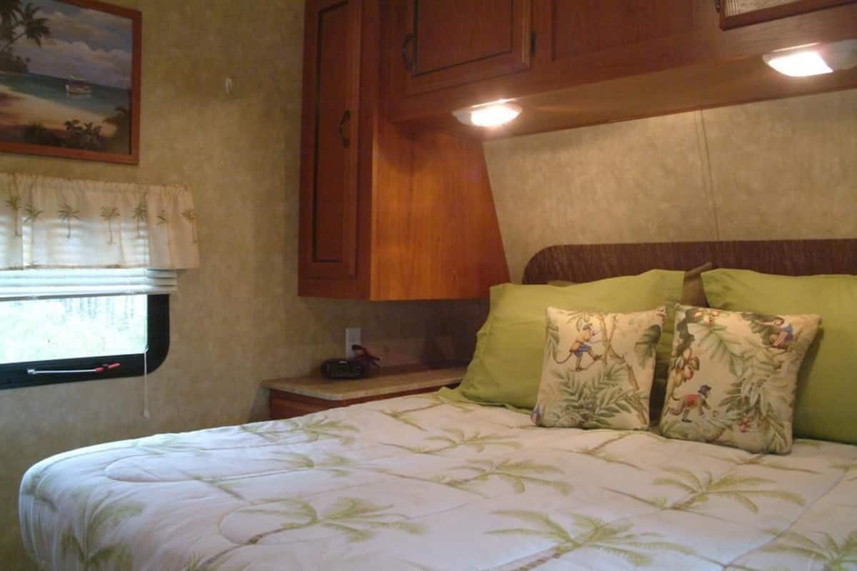 A bedroom with a bed, a window with curtains, wooden cabinets, and a nightstand.