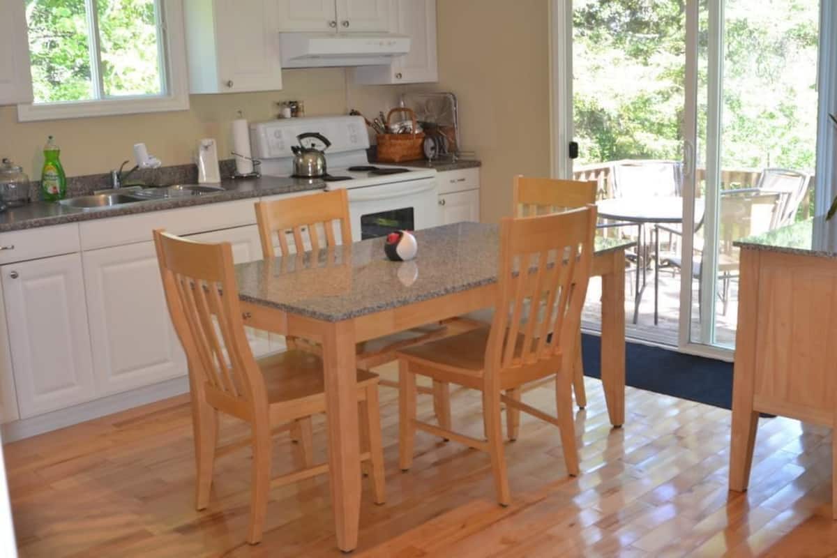 A kitchen with wooden chairs, a granite countertop, and a view of the outdoors.