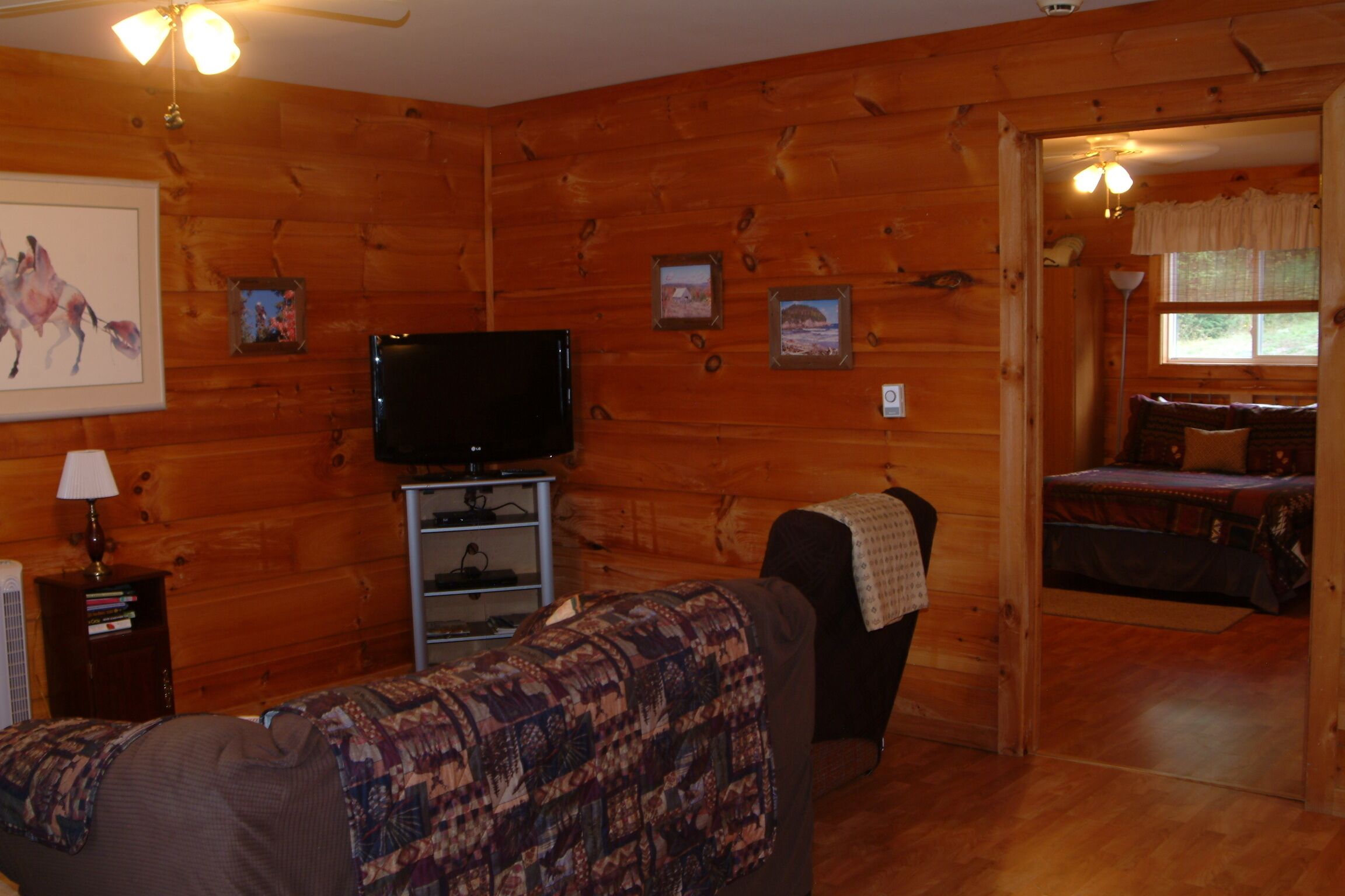 Ein gemütliches Blockhaus-Interieur mit Holzwänden, einem Fernseher auf einem Schrank, einer Couch und einem Bett mit Blick aus dem Fenster.