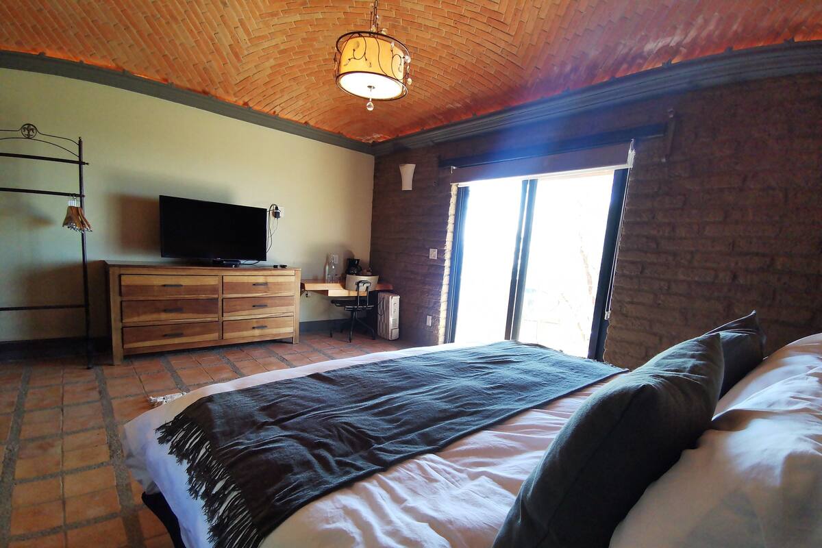 A bedroom with a large bed, a desk, a chair, a television, and a window.