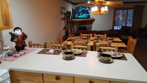 En matplats med ett stort bord dukat för en måltid, trästolar och en tv i bakgrunden.