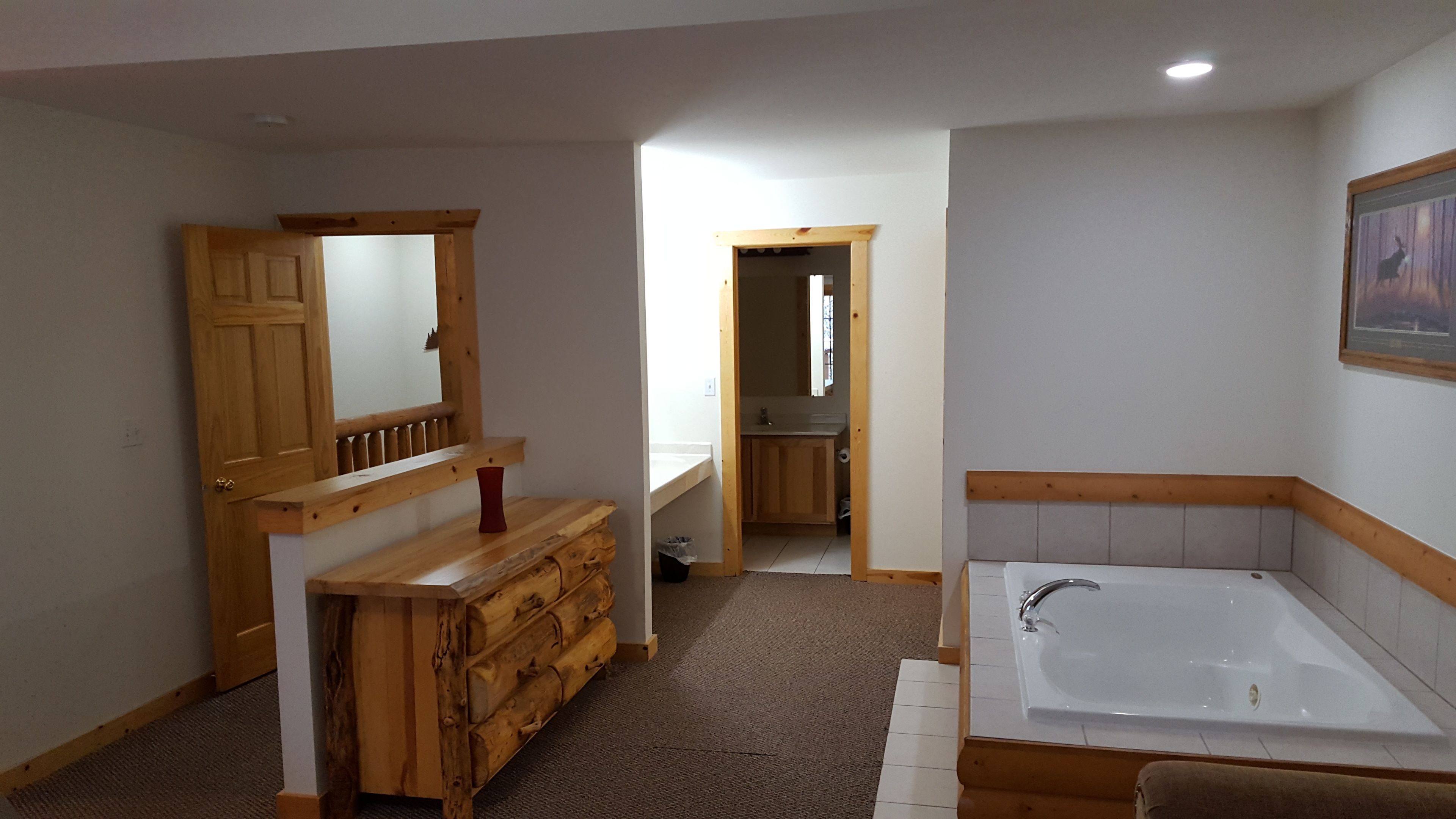 Un baño con tocador de madera, un espejo grande, una bañera y una puerta que da a otra habitación.