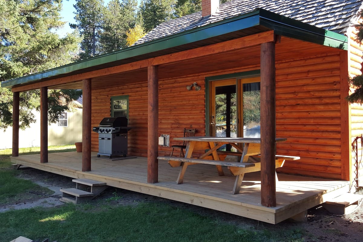 A wooden cabin with a covered porch, a grill, and a picnic table.
