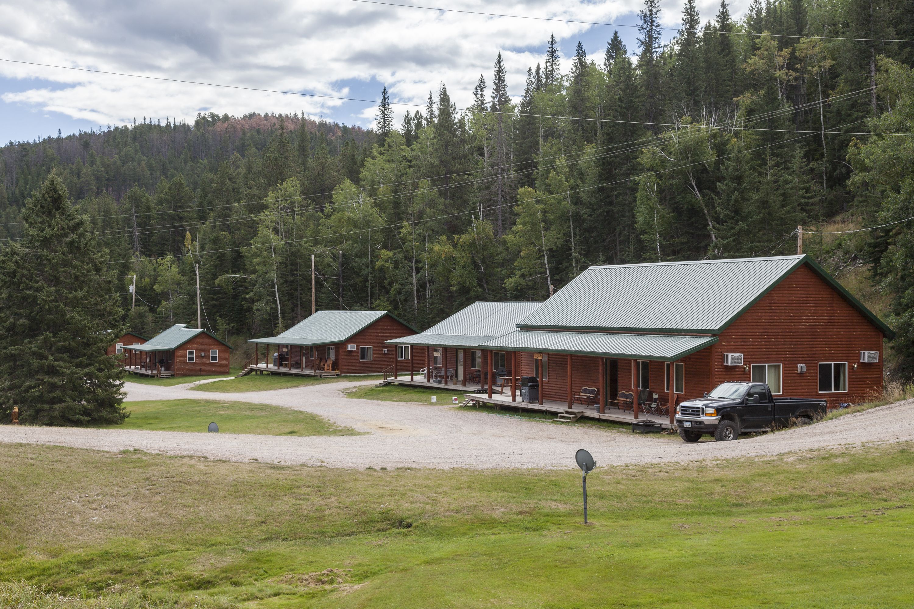 A row of rustic cabins with metal roofs, surrounded by a forested hillside.