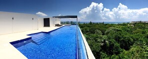A rooftop infinity pool with a clear view of the ocean and lush greenery. - Magnificent 3BR condo close to the Caribbean sea by Happy Ad (Playa del Carmen)