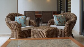 A cozy seating area with wicker chairs and a small table, featuring decorative cushions and a view of a dining area in the background. - Magnificent 3BR condo close to the Caribbean sea by Happy Ad (Playa del Carmen)
