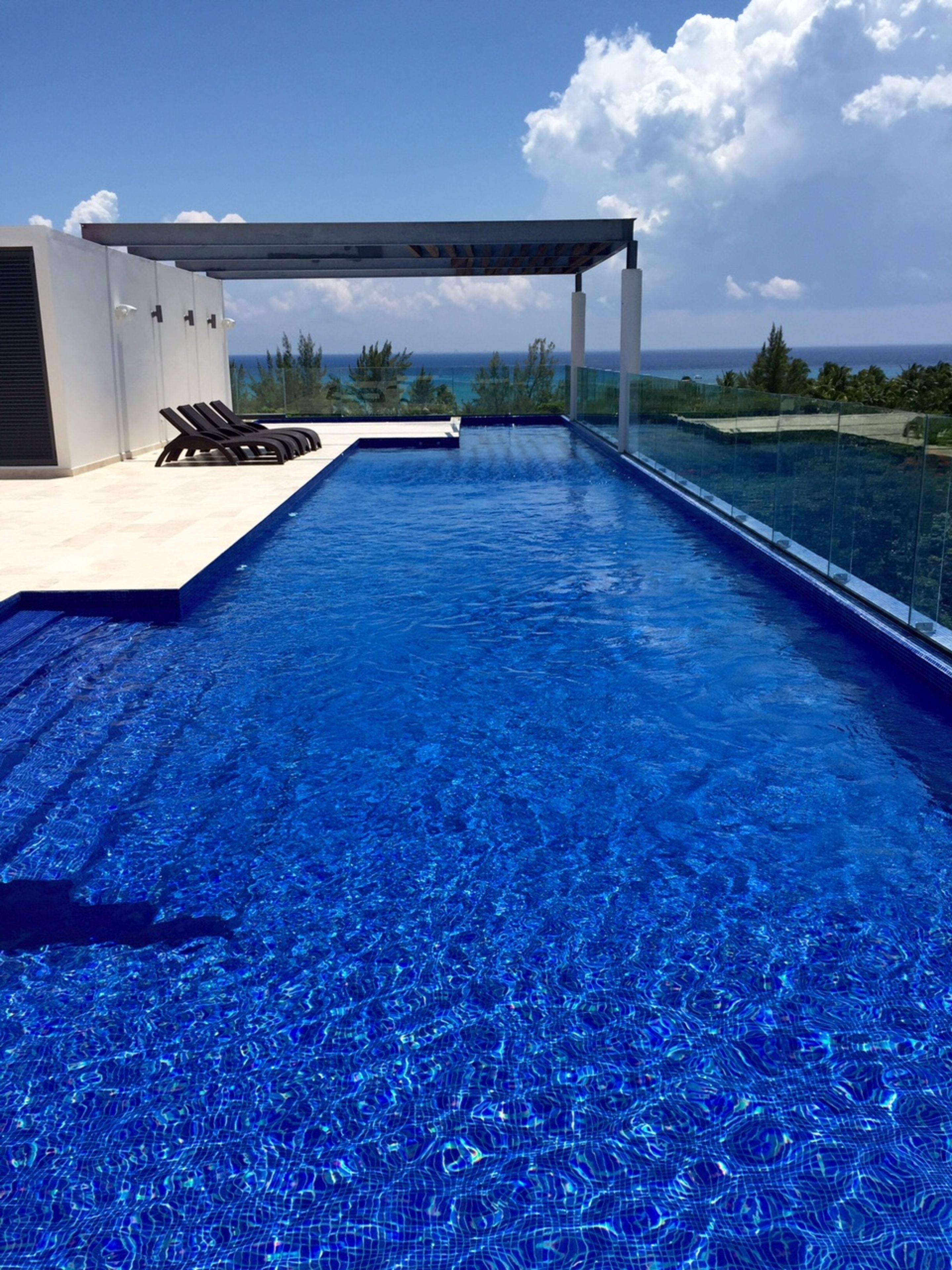 A modern infinity pool with clear blue water, a covered seating area, and a view of the ocean.