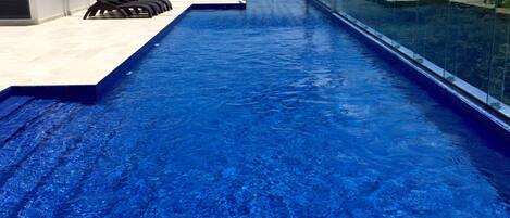 A modern infinity pool with clear blue water, a covered seating area, and a view of the ocean.