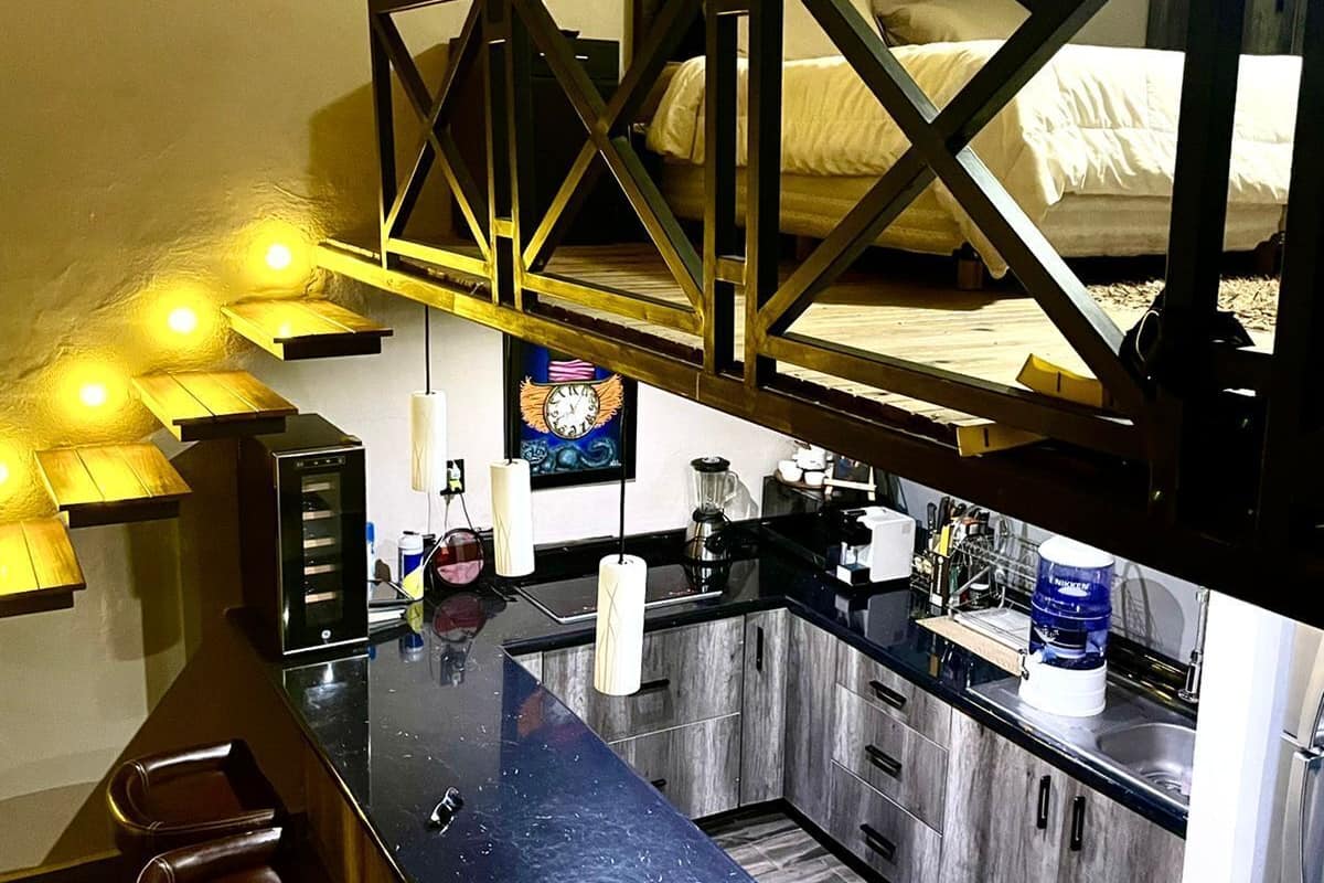 Une cuisine compacte avec un îlot central, des tabourets de bar et un lit en mezzanine.