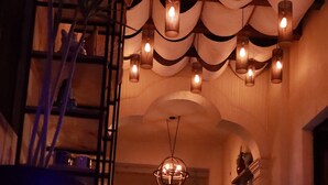 A dimly lit interior with a long, narrow, illuminated pathway, a chandelier, and a dining area with chairs and tables. - Independencia Dos 7 Hotel Boutique (Querétaro)