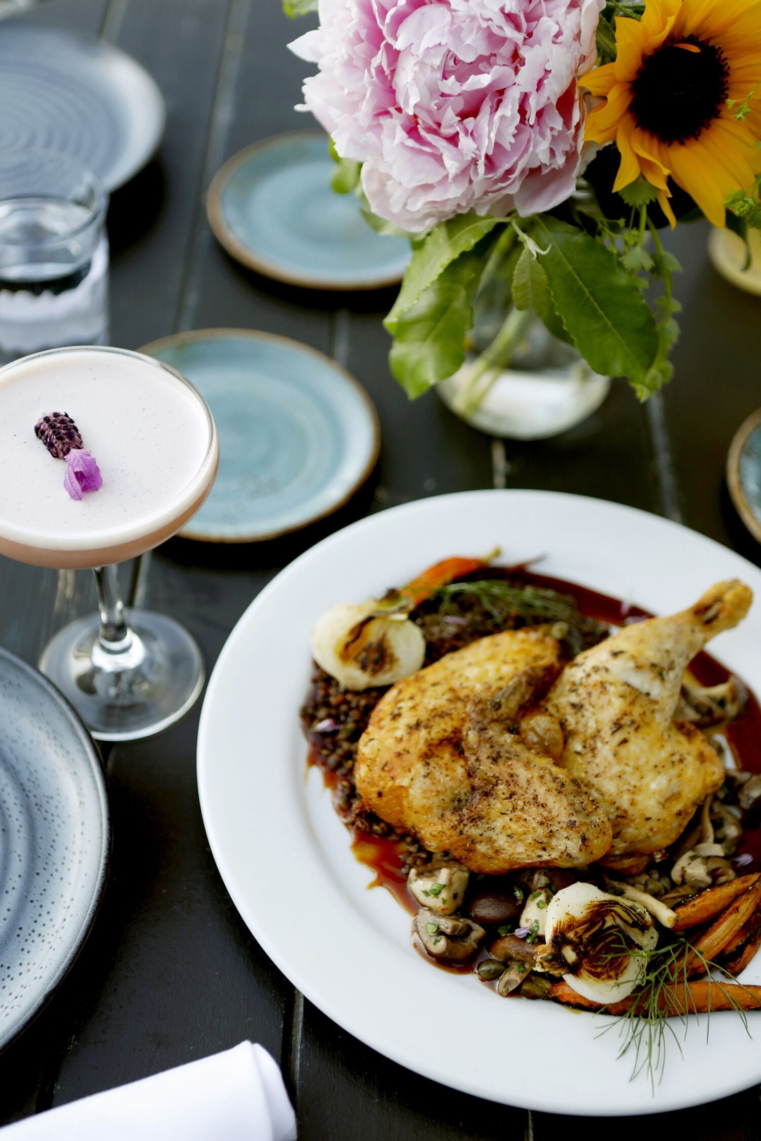 Una mesa de comedor con platos de comida, un vaso de bebida y un jarrón con flores.