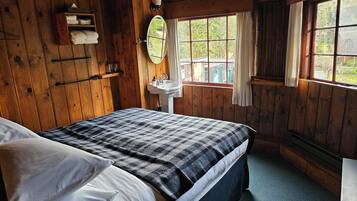 A wooden cabin bedroom with a bed, a sink, a window, and a mirror.