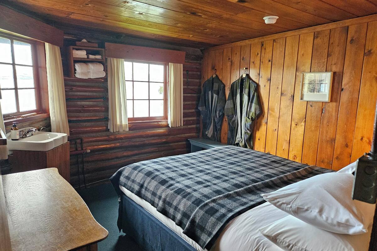 A wooden cabin room with a bed, a sink, and a window.
