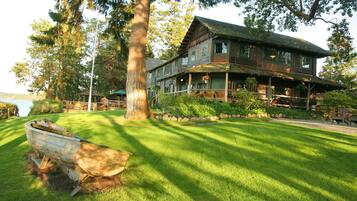 A large wooden house with a porch, surrounded by a well-maintained lawn and trees.