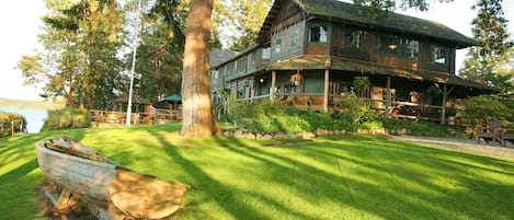 A large wooden house with a porch, surrounded by a well-maintained lawn and trees.