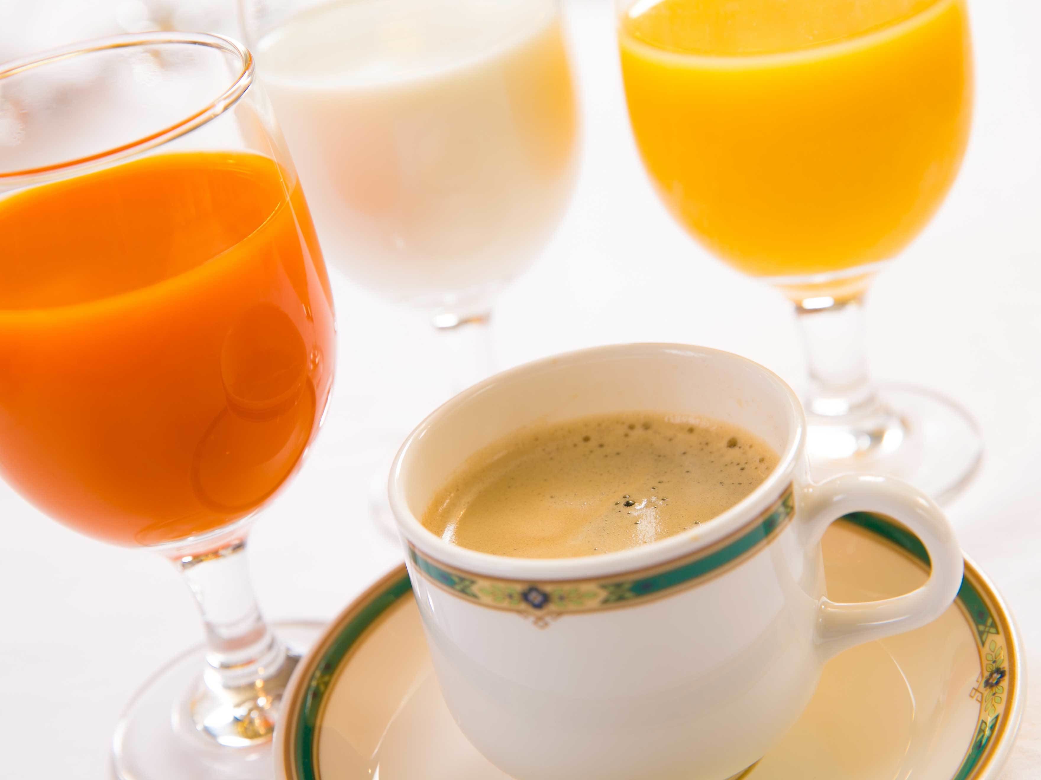 A cup of coffee on a saucer with a decorative rim, accompanied by two glasses of orange juice.