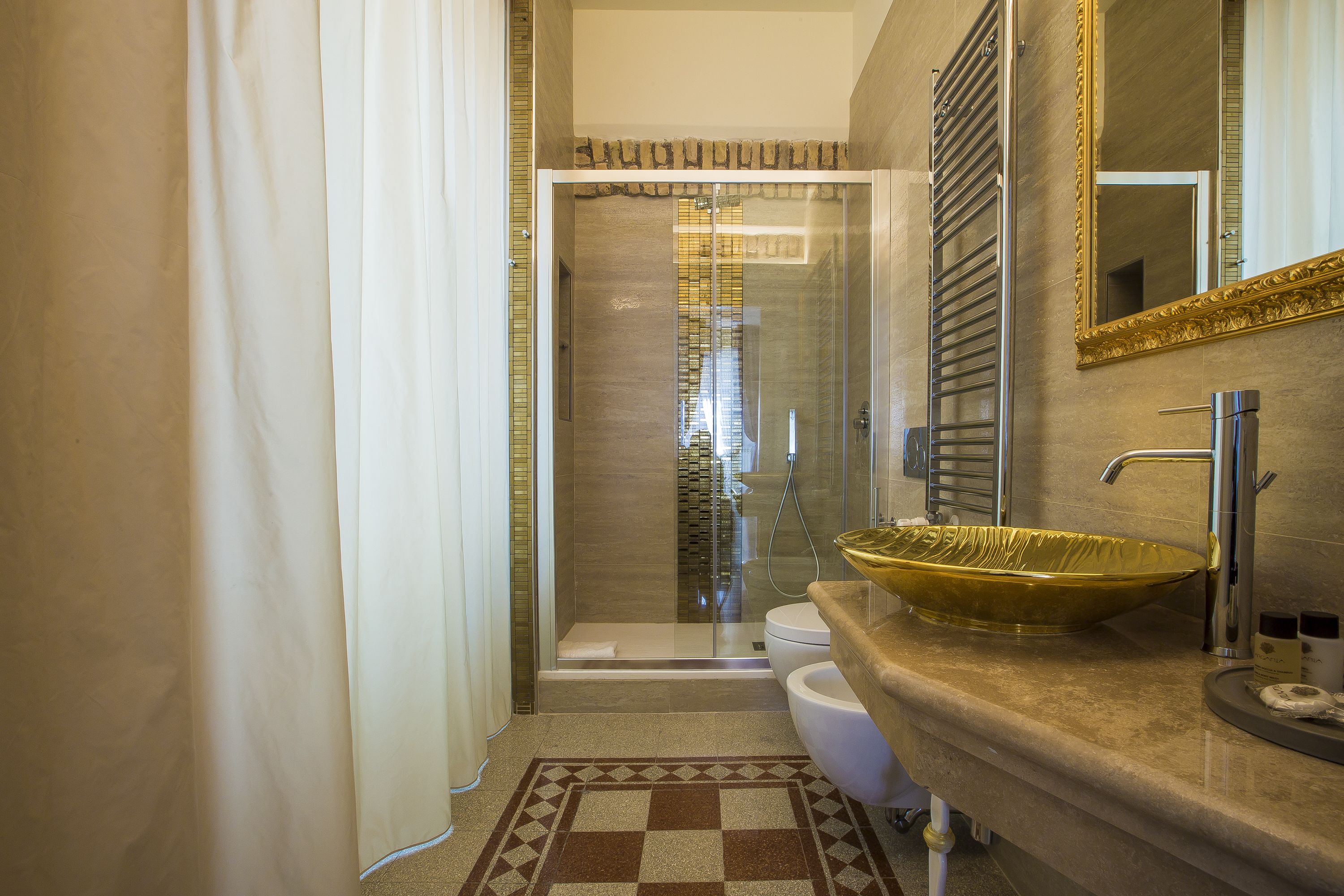 A modern bathroom with a glass shower enclosure, a beige tiled floor, and a large mirror with a gold frame.