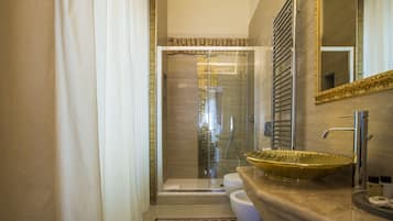 A modern bathroom with a glass shower enclosure, a beige tiled floor, and a large mirror with a gold frame.