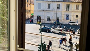 A balcony with a view of a street, a pharmacy, and parked cars. - Trastevere Royal Suite (Rome)