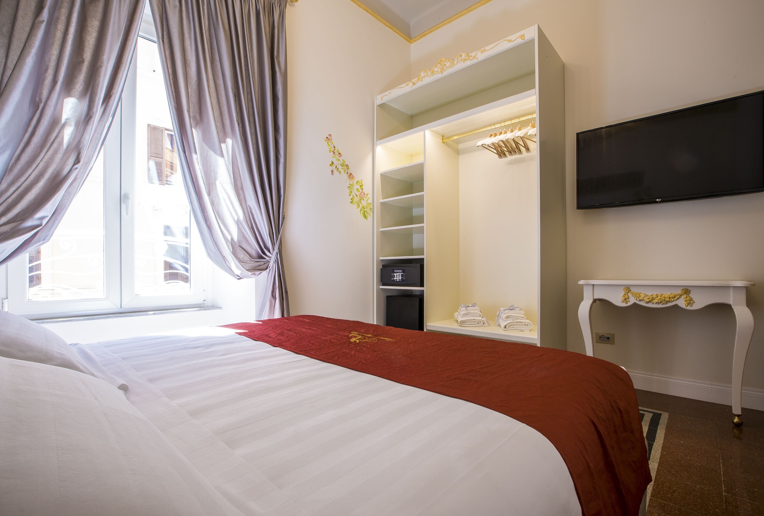 Een hotelkamer met een bed, een televisie, een kledingkast en een raam met gordijnen.
