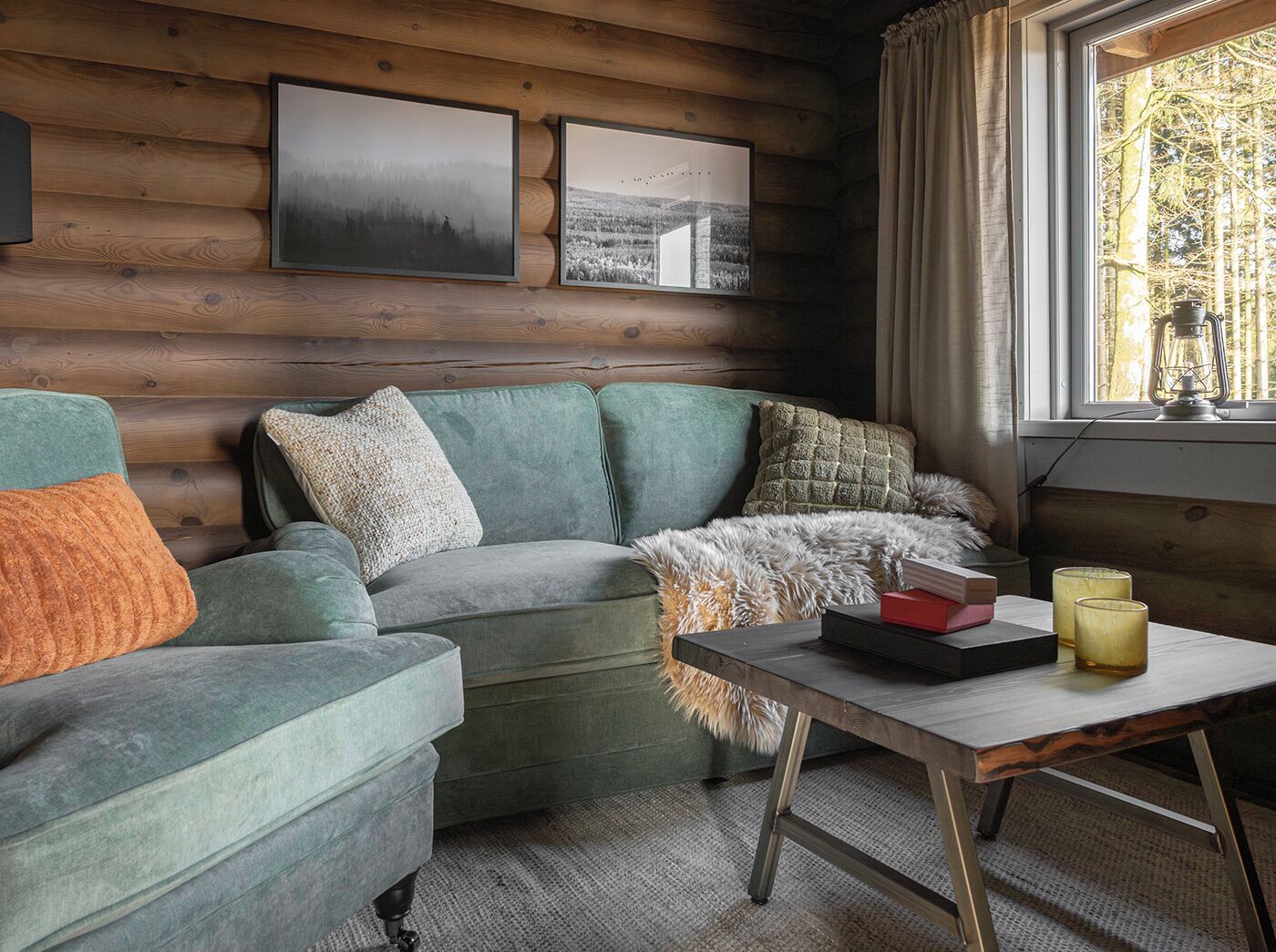 Interior acogedor de una cabaña de troncos con un sofá verde, una mesa de madera y cuadros en la pared.