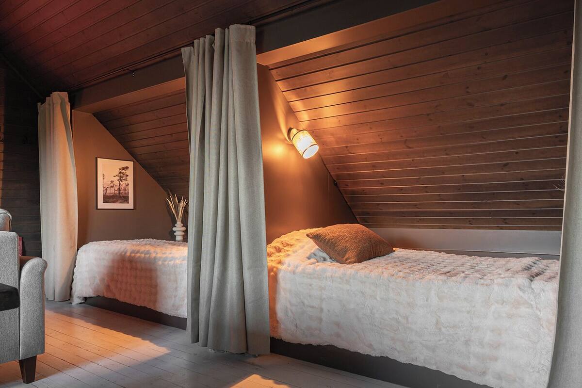 Ein gemütliches Schlafzimmer mit zwei Betten, Holzbalken an der Decke und einer Wandleuchte.
