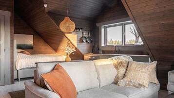 A cozy loft bedroom with a sloped ceiling, a sofa, a bed, and a window overlooking greenery.