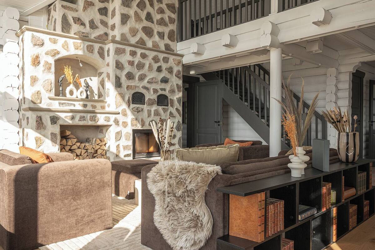 Ein gemütliches Wohnzimmer mit Kamin aus Stein, einer Treppe und einem Bücherregal voller Bücher und Dekoration.