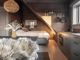 Un dormitorio acogedor con un ventanal grande, techo de madera y una zona de cocina con electrodomésticos modernos.