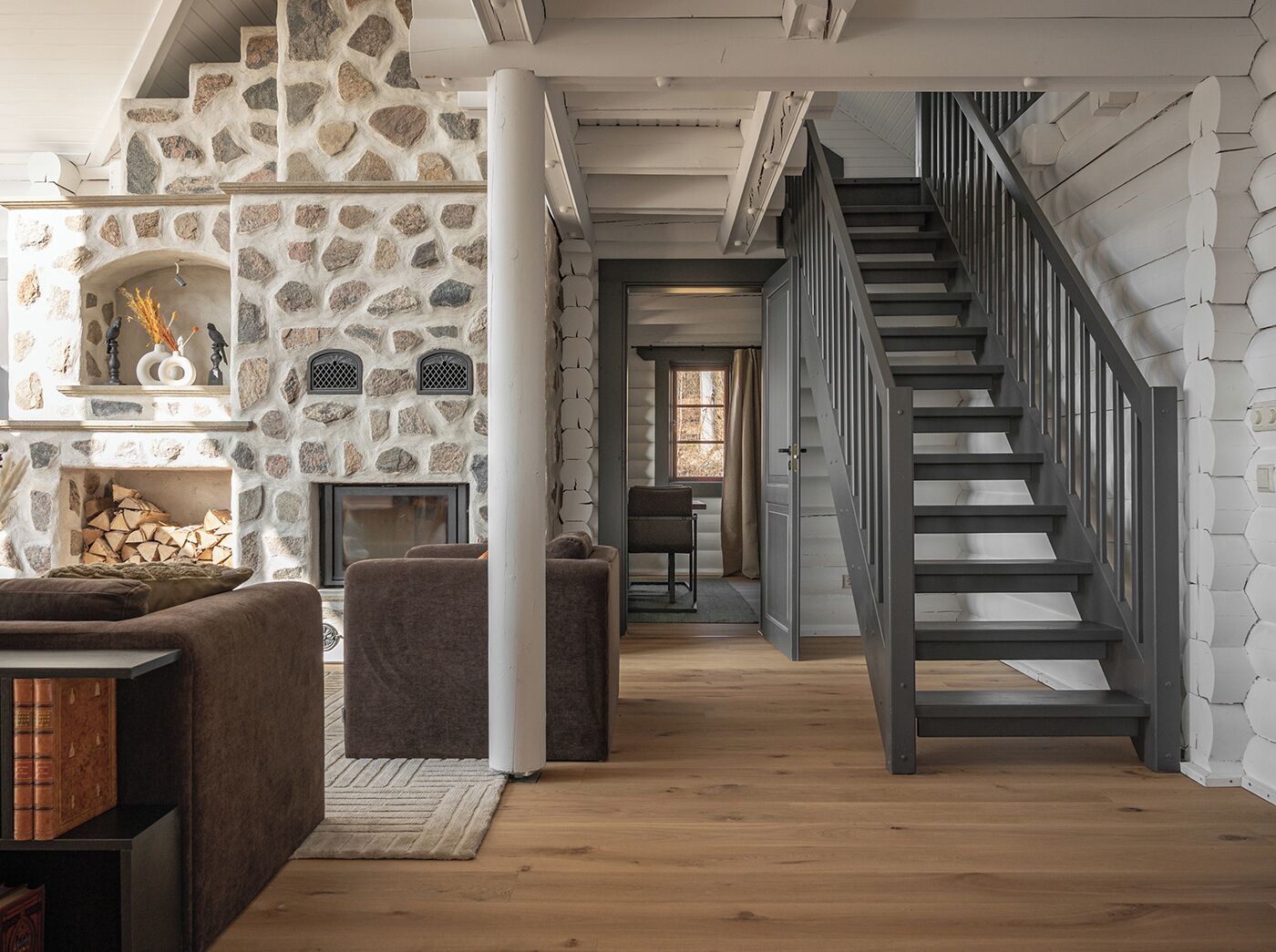 Ett mysigt vardagsrum med en öppen spis i sten, en trappa och en modern design.