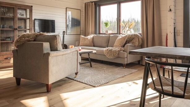 A cozy living room with a sofa, armchair, and coffee table, a television, and a window with curtains.