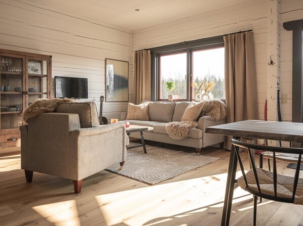 A cozy living room with a sofa, armchair, and coffee table, a television, and a window with curtains.