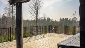 A wooden deck with a black metal railing, surrounded by trees and a clear sky.