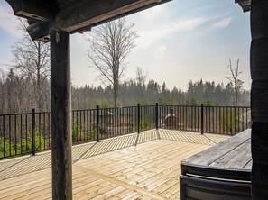 A wooden deck with a black metal railing, surrounded by trees and a clear sky.