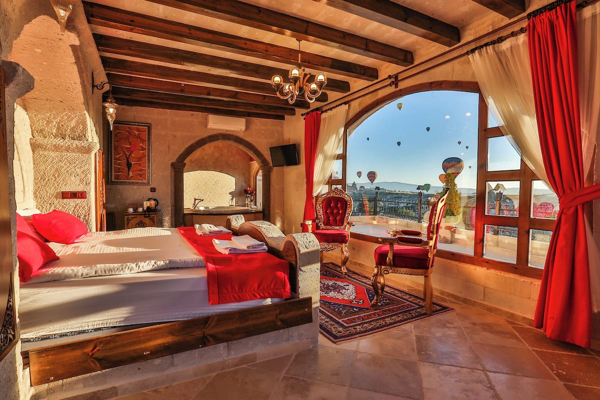 A bedroom with a large bed, a red chair, a small table, and a view of hot air balloons.