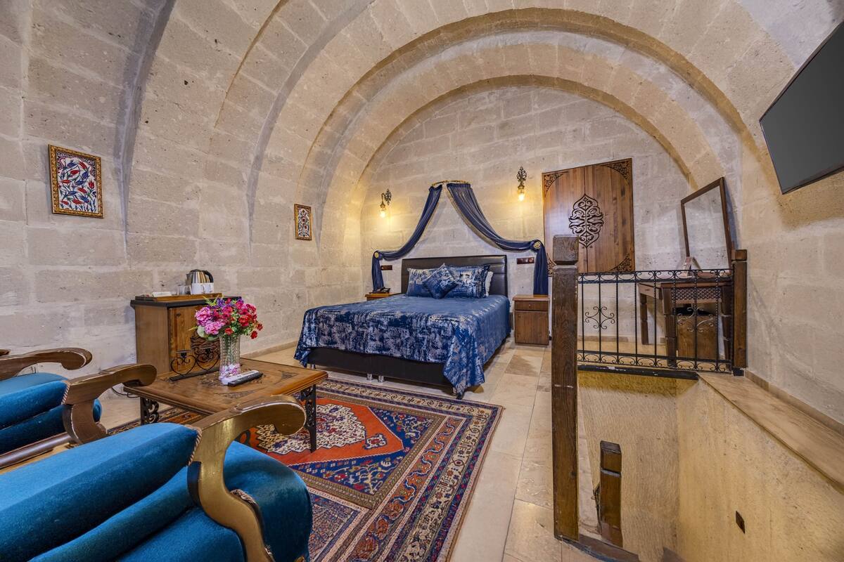 A bedroom with a four-poster bed, a wooden desk, a chair, a rug, and a staircase.