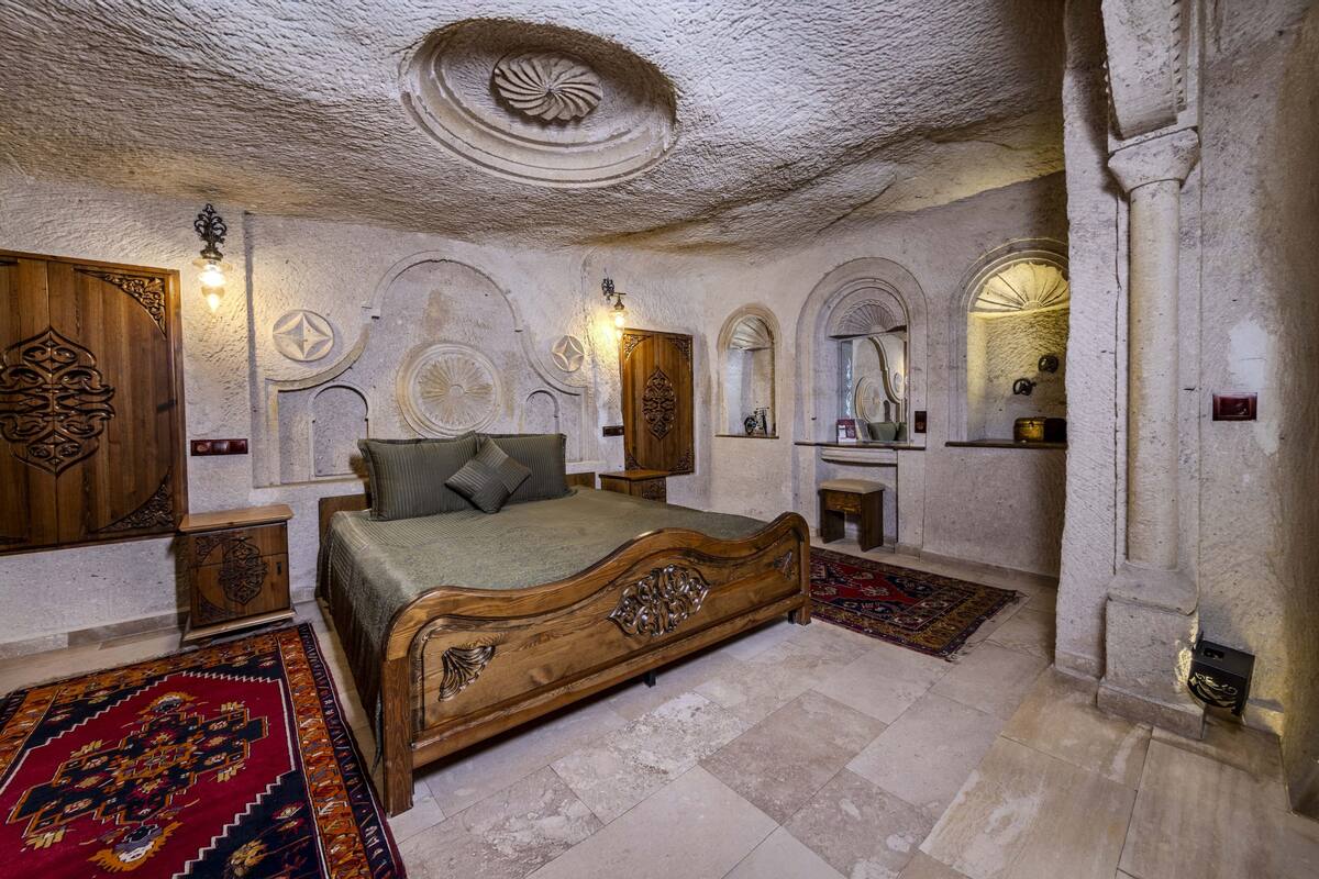 A bedroom with a wooden bed, a red carpet, and stone walls.
