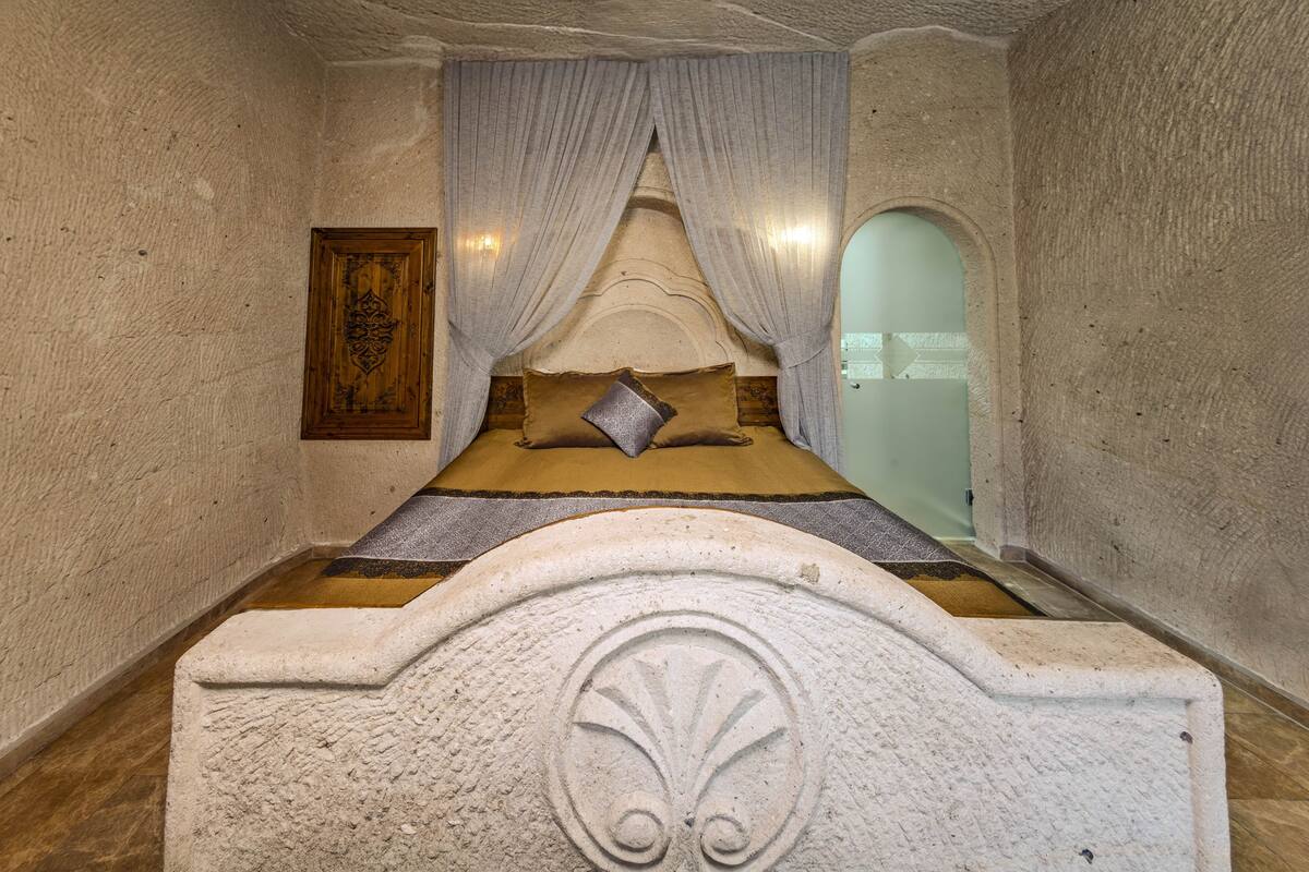 A bedroom with a stone headboard, a bed with a pillow, and a curtain.