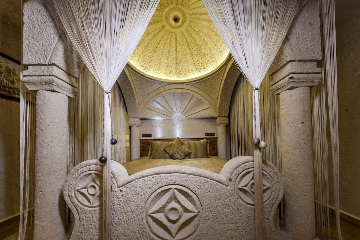 A room with a bed centered under a dome-shaped ceiling, flanked by columns and draped curtains.
