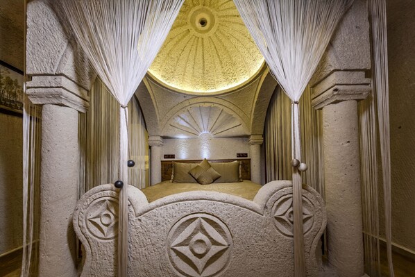 A room with a bed centered under a dome-shaped ceiling, flanked by columns and draped curtains. - Cappadocia Inn Cave Hotel (Nevsehir)