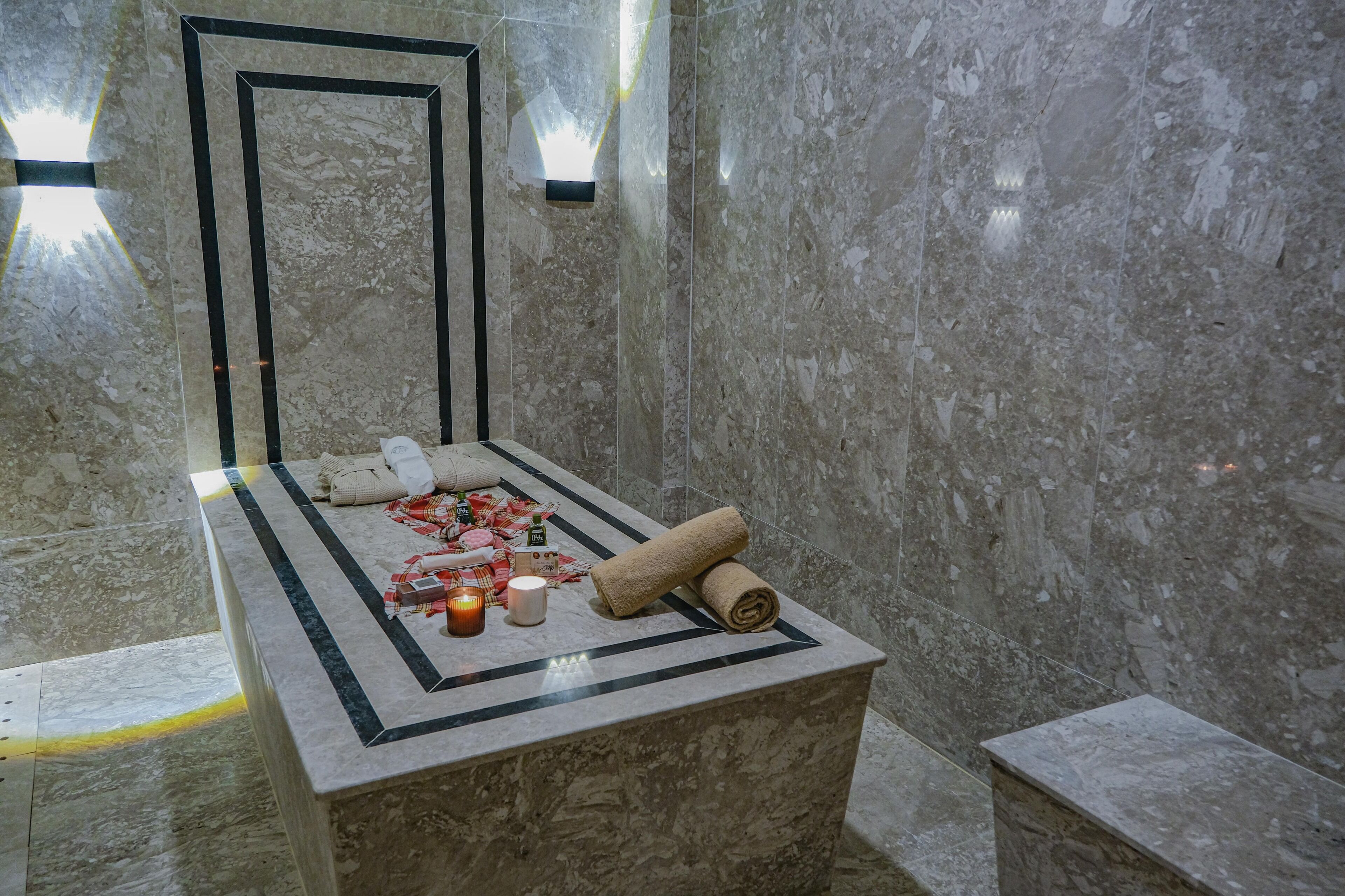 A marble-tiled bathroom with a bench, candles, and towels.