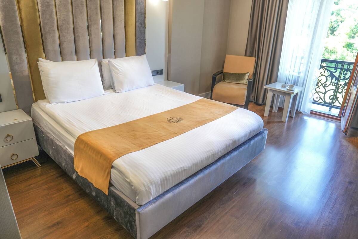 A large bed with a wooden headboard, a bedside table, a chair, and a small table with a lamp.