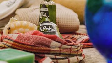 Una botella de aceite de oliva, una pastilla de jabón verde, un vaso azul y un paño escocés sobre una superficie texturizada.