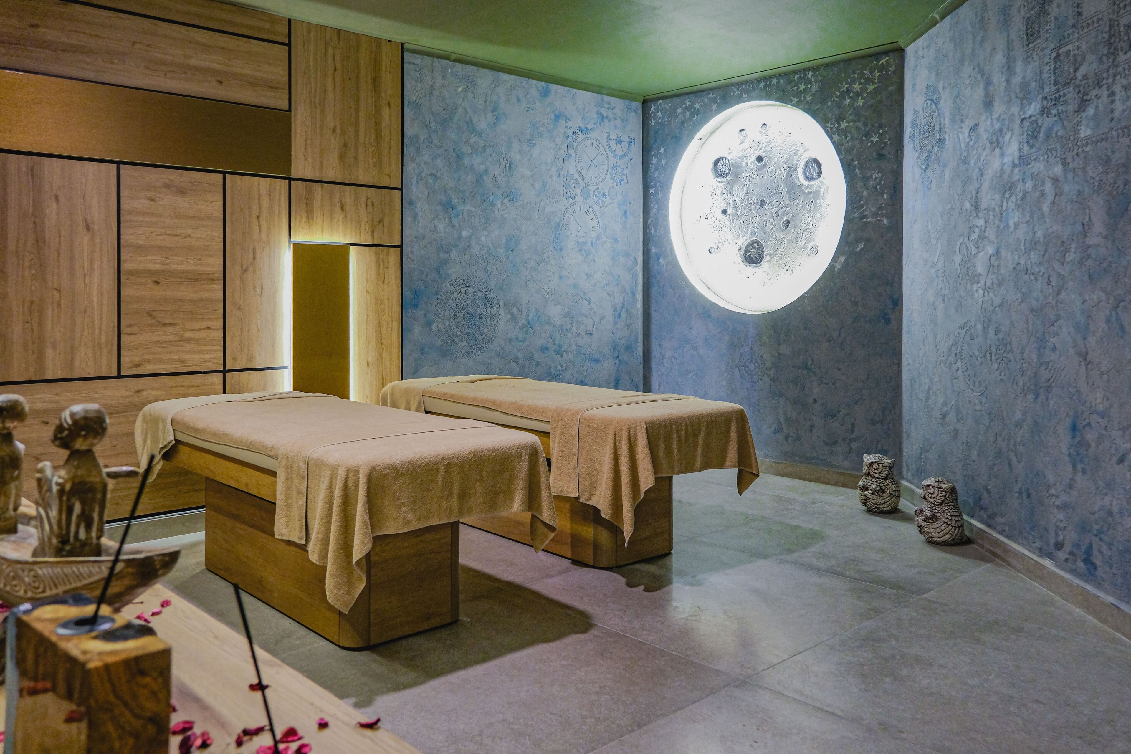 Un cuarto de spa con dos camillas de tratamiento, un mural de la luna en la pared y un revestimiento de panel de madera.