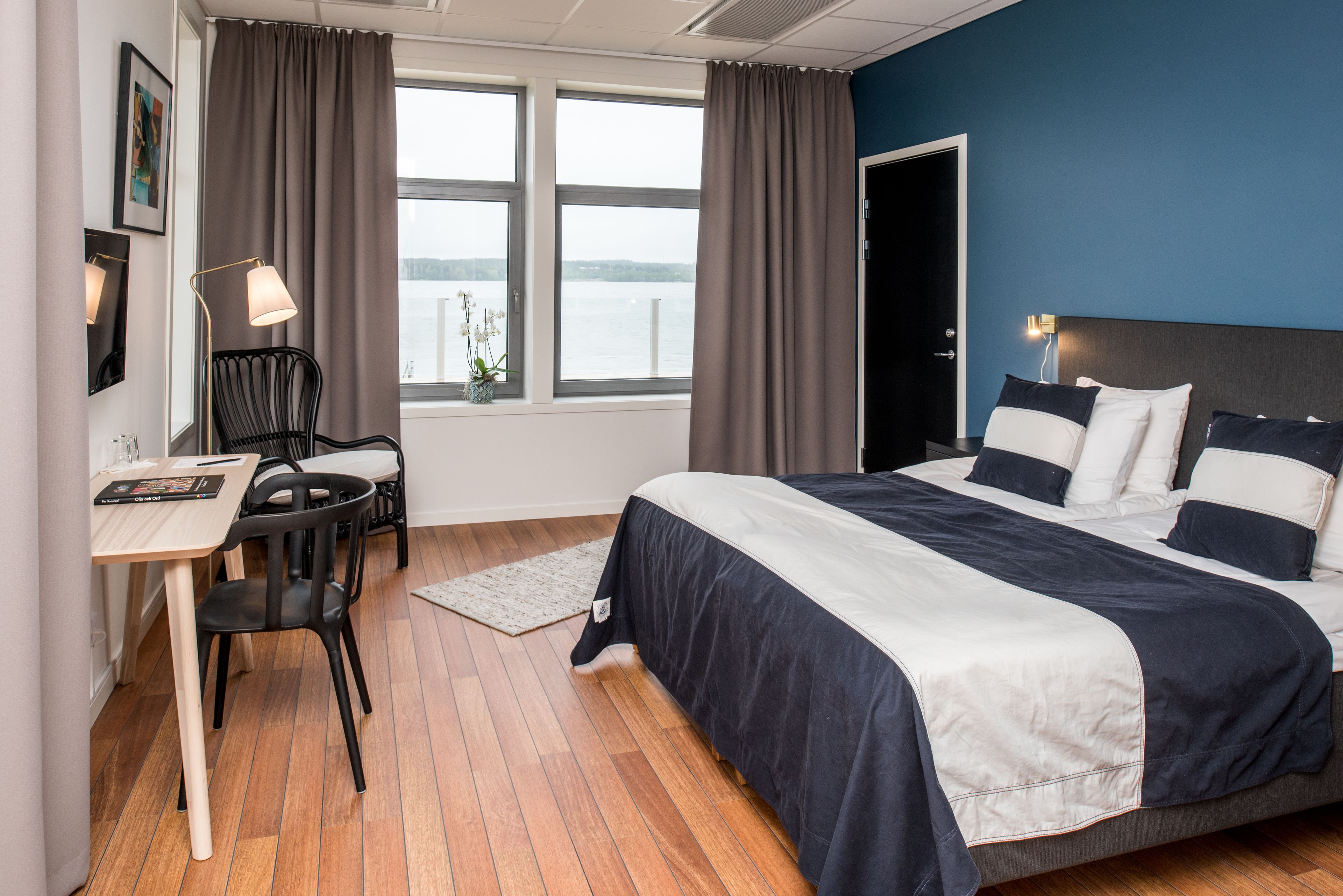 Una habitación de hotel con cama, escritorio, silla y ventana con cortinas.